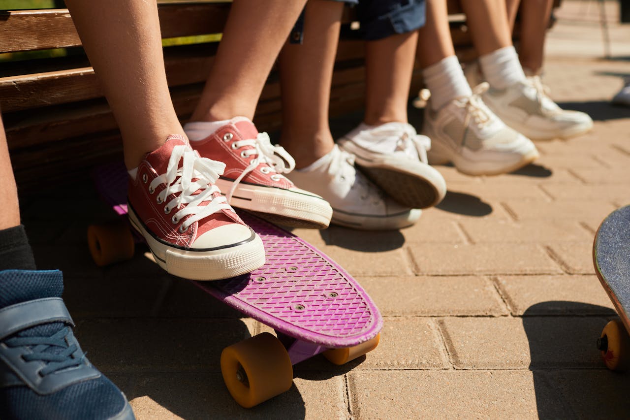 Close-up of childrens feet in sneakers with skateboards in a sunny park.