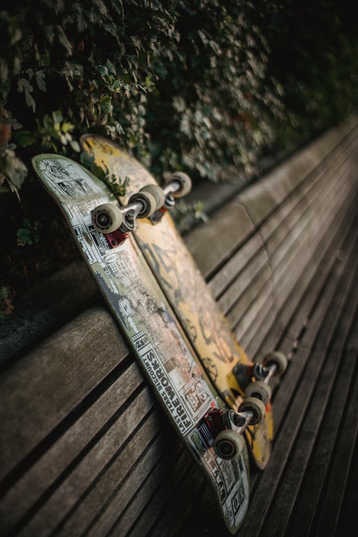 Two skateboards leaning against a wooden park bench with lush foliage in the background.